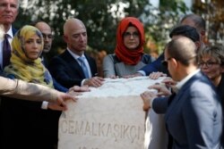 Hatice Cengiz, centre, the fiancee of slain Saudi journalist Jamal Kashoggi, accompanied by his colleagues, W. Post owner Jeff Bezos, unveil a plaque, near the Saudi Arabia consulate in Istanbul, marking the anniversary of his death, Oct. 2, 2019.