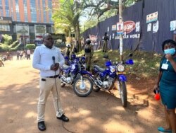 A Ugandan journalist reports live from a scene where journalist walked out in protest of security brutality with. police and army officers stand behind him. (Halima Athumani/VOA)