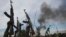 Rebel fighters hold up their rifles as they walk in front of a bushfire in a rebel controlled territory in Upper Nile State, South Sudan, Feb. 13, 2014. 