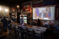 A few visitors and staff of a pub watch the broadcast of Russian President Vladimir Putin's address to the nation, in Moscow, Russia, March 25, 2020.