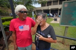 Myrna and Abraham Ah Hee react as they stand in front of an evacuation center at the War Memorial Gymnasium, Thursday, Aug. 10, 2023, in Wailuku, Hawaii. The Ah Hees were there because they were looking for Abraham's brother. Their own home in Lahaina was spared, but the homes of many of their relatives were destroyed by wildfires. They haven't been able to get in touch with Abraham's brother. (AP Photo/Rick Bowmer)