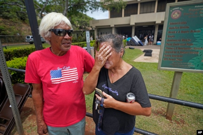 Myrna and Abraham Ah Hee react as they stand in front of an evacuation center at the War Memorial Gymnasium, Thursday, Aug. 10, 2023, in Wailuku, Hawaii. The Ah Hees were there because they were looking for Abraham's brother. Their own home in Lahaina was spared, but the homes of many of their relatives were destroyed by wildfires. They haven't been able to get in touch with Abraham's brother. (AP Photo/Rick Bowmer)