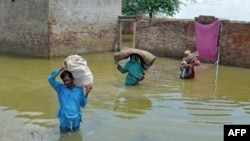 Una familia desplazada por las inundaciones lleva sus pertenencias mientras caminan por las áreas inundadas después de las fuertes lluvias monzónicas en Sohbatpur, en el distrito de Jaffarabad, provincia de Baluchistán, el 19 de agosto de 2024.