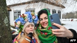 A woman and a young girl, wearing traditional Ukrainian clothes, pose for selfie photographs as they take part in Christmas celebrations in the village of Pyrogove, near Kyiv on December 25, 2023, amid Russian invasion in Ukraine.