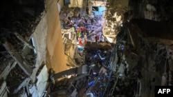 An photo taken on July 30, 2024, shows rescuers on the street near a building with destroyed top floors following an Israeli military strike on Beirut's southern suburb.