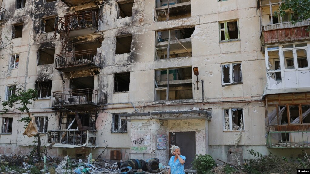 一位当地妇女站在北顿涅茨克严重破坏的居民楼前。(photo:VOA)