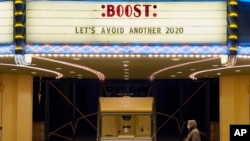 FILE - A man walks underneath the marquee of the Alex Theatre in Glendale, Calif., which bears a message urging people to get COVID-19 vaccine booster shots, Jan. 24, 2022.