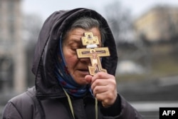 A religious woman holds a cross as she prays on Independence square in Kyiv in the morning of February 24, 2022. (Photo by Daniel LEAL / AFP)