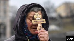 一位女士在基辅独立广场举着十字架在晨间祷告。(2022年2月24日)