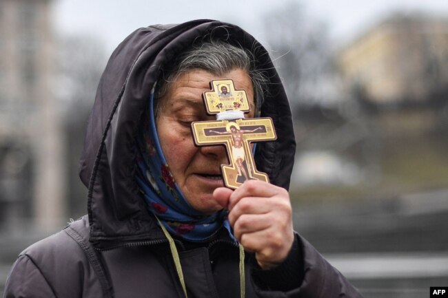 A religious woman holds a cross as she prays on Independence square in Kyiv in the morning of February 24, 2022. (Photo by Daniel LEAL / AFP)