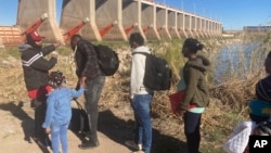 FILE - A Mexican smuggler guides a Haitian family across the Morelos Dam over the Colorado River from Los Algodones, Mexico, on Feb. 4, 2022, to Yuma, Ariz., on the other side.