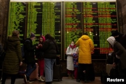 People stand in front of the train schedule at Central Railway Station as they try to leave city of Kyiv, Ukraine, Feb. 24, 2022.