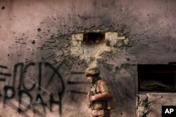 A Ukrainian serviceman walks by a building which was hit by a large caliber mortar shell in the frontline village of Krymske, Luhansk region, in eastern Ukraine, Feb. 19, 2022.