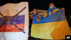 Ukrainians hold up their country's flag, right, as they attend a patriotic action 'Mariupol is Ukraine' in Mariupol, Ukraine, Feb. 22, 2022.