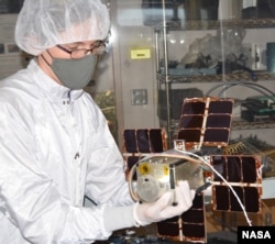 A researcher holds the NACHOS instrument, which is fixed to a CubeSat with its solar panels unfolded. (Photo Credit: Los Alamos National Laboratory/Logan Ott/NASA)