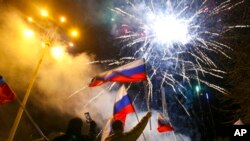 Sekelompok orang mengibarkan bendera Rusia dalam perayaan pengakuan wilayah Donestk sebagai republik independen oleh Rusia pada 21 Februari 2022. Donetsk merupakan wilayah di Ukraina timur yang dikuasai oleh kelompok separatis pro-Rusia. (Foto: AP/Alexei Alexandrov)