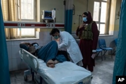 FILE - A doctor looks after a patient as a Taliban member stands behind him in Wazir Mohammad Akbar Khan National Hospital, in Kabul, Afghanistan, Dec. 5, 2021.