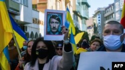 反战抗议人士在俄罗斯驻马其顿首都斯科普里的大使馆外示威，他们打着乌克兰旗帜，并举着把普京描绘为希特勒的图像。(2022年2月25日)
