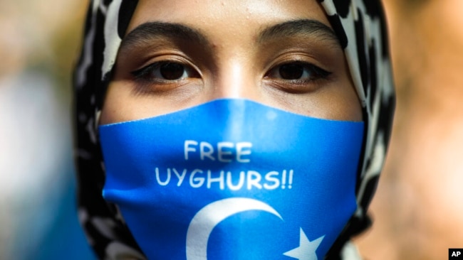 FILE - A woman wears a face mask reading 'Free Uyghurs' as she attends a protest during the visit of Chinese Foreign Minister Wang Yi in Berlin, Sept. 1, 2020.