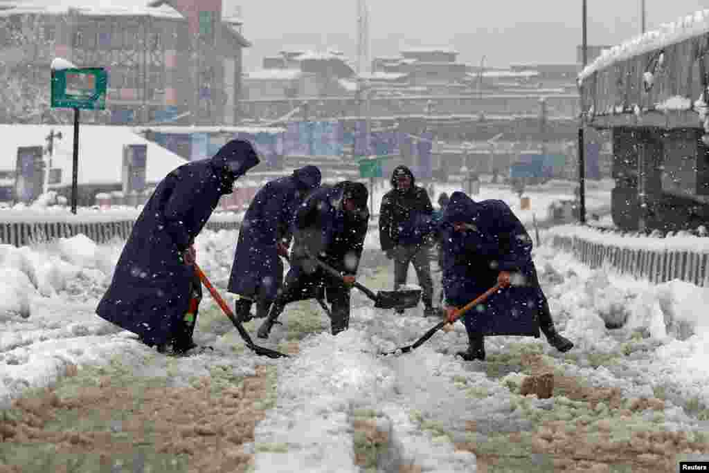 Municipal workers use shovels to remove snow from a road during snowfall in Srinagar, Indian-controlled Kashmir.