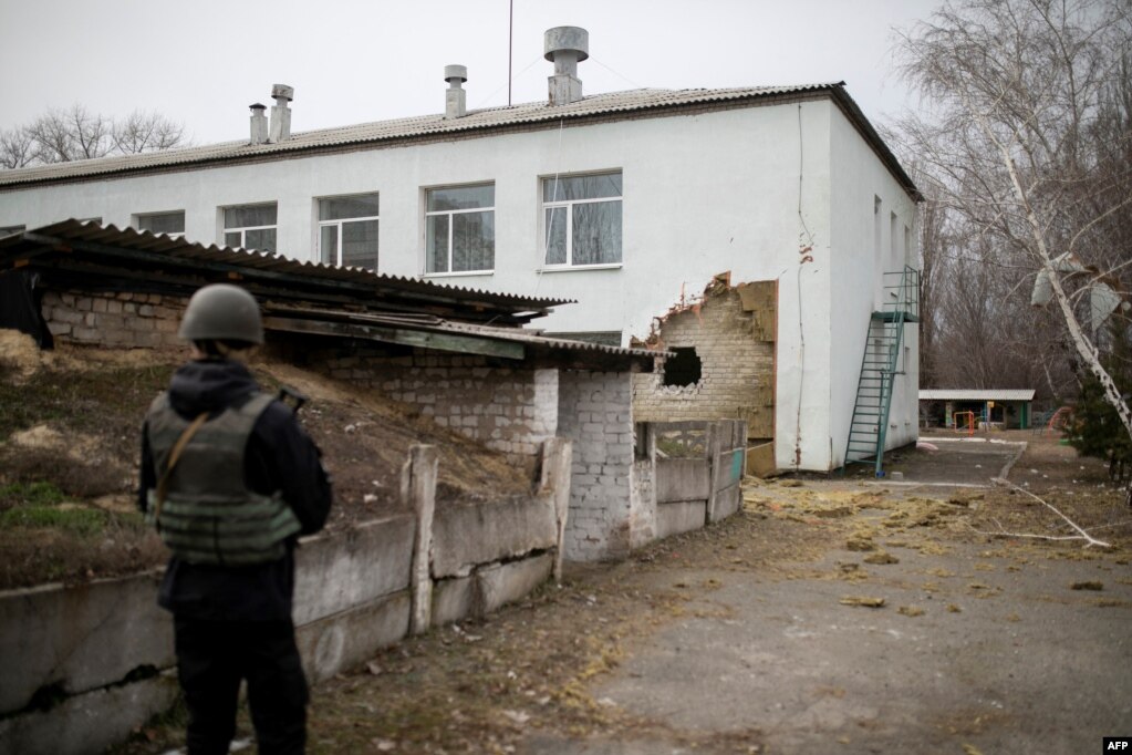 在乌克兰卢甘斯克州的斯塔尼齐亚卢甘西卡，一名乌克兰军人站在据报道因遭炮击而受损的幼儿园建筑边。(2022年2月17日)(photo:VOA)