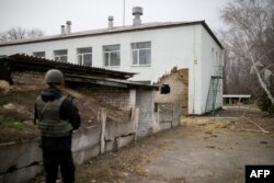 A Ukrainian soldier stands next to a damaged building housing a kindergarten after it was reportedly shelled, in the town of Stanytsia Luhanska, Luhansk region, Ukraine, Feb. 17, 2022.