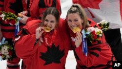 Canada goalkeeper Emerance Maschmeyer and Natalie Spooner, right, pose with their gold medals after defeating the United States in during the women's gold medal hockey game at the 2022 Winter Olympics, Feb. 17, 2022, in Beijing.