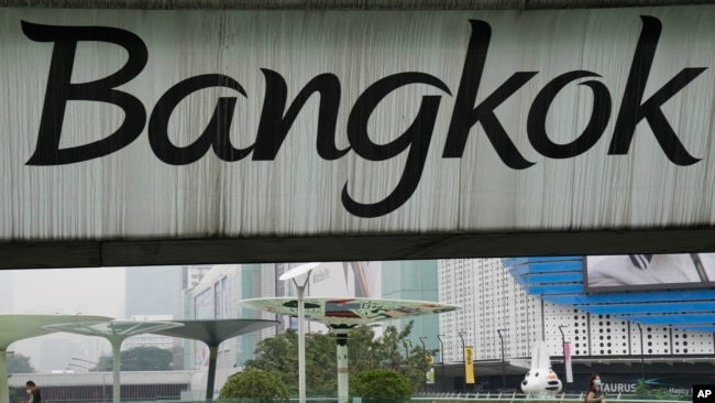 People walk on an elevated pathway under the "Bangkok" sign written on the SkyTrain track in Bangkok, Thailand, on Thursday, Feb. 17, 2022. (AP Photo/Sakchai Lalit)