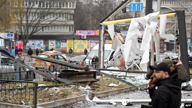 Polisi dan petugas keamanan berkumpul di dekat puing-puing peluru yang mendarat di jalanan kota Kyiv, Ukraina, pada 24 Februari 2022. (Foto: AFP/Sergei Supinsky)