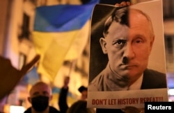 پرتره‌ای از نصف صورت هیتلر و پوتین در دست یک معترض ضدجنگ در بارسلون، اسپانیا، که زیرش نوشته شده «نگذارید تاریخ تکرار شود!!!» ۵ اسفند ۱۴۰۰