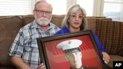 Joey and Paula Reed pose for a photo with a portrait of their son Marine veteran and Russian prisoner Trevor Reed at their home in Fort Worth, Texas, Feb. 15, 2022. Russia is holding Trevor Reed, who was sentenced to nine years on charges he assaulted a p
