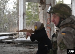 FILE - A woman holds a replica of a Kalashnikov rifle during a military drill of the Ukrainian Territorial Defense Forces, the military reserve of the Ukrainian Armed Forces, outside Kyiv, Feb. 19, 2022.