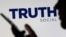El logotipo de la red social Truth se muestra detrás de una mujer que sostiene un teléfono inteligente en esta ilustración tomada el 21 de febrero de 2022.