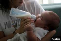 FILE - A mother feeds her baby with a bottle in Caracas, June 17, 2013.