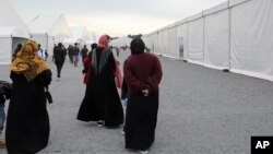 Afghan refugees walk alongside temporary housing in Liberty Village at Joint Base McGuire-Dix-Lakehurst in Trenton, New Jersey, Dec. 2, 2021. The U.S. government now plans to consolidate sites like this into one in northern Virginia. 