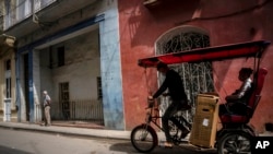 Con máscara en medio de la pandemia de COVID-19, un hombre transporta a un cliente en un taxi-bicicleta en La Habana, Cuba, el miércoles 16 de febrero de 2022.
