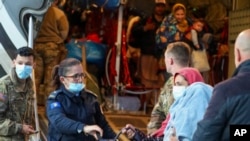 FILE - In this image provided by the US Army, US military personnel, and Kosovo security officials help Afghan refugees after their arrival at the Pristina International Airport in Kosovo on Oct. 16, 2021.