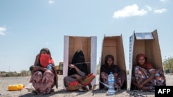 Sejumlah perempuan duduk di dalam kardus yang bertuliskan UNHCR ketika menunggu untuk didaftarkan kepada pihak berwenang di halaman Hotel Agda di Kota Semera, Ethiopia, pada 14 Februari 2022. (Foto: AFP/Eduardo Soteras)