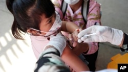 A young girl held by her mother pushes a shaft of a needle as she receives the first dose of Sinovac's COVID-19 vaccine at a health center outside Phnom Penh, Cambodia on Wednesday, Feb. 23, 2022. (AP Photo/Heng Sinith)