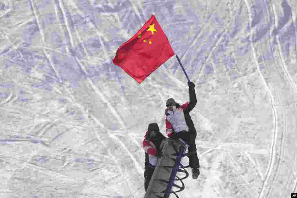 Voluntarios se suben a un cañón de nieve y sostienen una bandera china, donde se celebran los Juegos Olímpicos de Invierno de 2022.