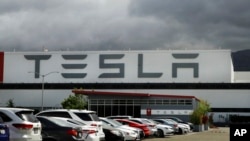 FILE - Vehicles are parked outside the Tesla plant, in Fremont, Calif., May 12, 2020. 