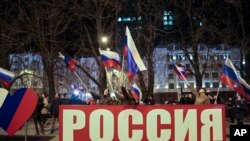 Gente ondea banderas nacionales rusas para celebrar, en el centro de Donetsk, el territorio controlado por militantes prorrusos, en el este de Ucrania, el lunes 21 de febrero de 2022 por la noche.