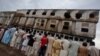 FILE - Residents stand outside a garment factory that caught fire the day before, in Karachi, Sept. 13, 2012. 