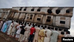 FILE - Residents stand outside a garment factory that caught fire the day before, in Karachi, Sept. 13, 2012. 