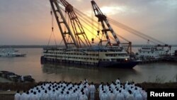 FILE - Rescue workers stand on the river bank as the capsized cruise ship Eastern Star is pulled out of the Yangtze against sunset, in Jianli, Hubei province, China, June 5, 2015.