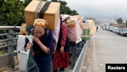 FILE - Moroccan women carry goods to be taken across the border from Spain's North African enclave of Melilla into Moroccan settlement of Beni Ansar, in Melilla, Spain, July 18, 2017.