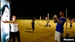 Seorang perempuan berfoto di depan gambar pesebakbola Uruguay, Luis Suarez yang memperlihatkan deretan giginya, di Pantai Copacabana, Rio de Janeiro (26/6),