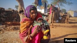 Seorang anak berumur 14 tahun sedang duduk menggendong bayinya yang berumur 4 bulan di luar rumahnya di desa dekat Baran di barat laut India, 21 Januari 2013. 