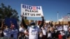 FILE - Migrants from Central America and other nationalities, hoping to cross and request asylum in the U.S., hold banners and shout slogans to U.S. President Joe Biden at their campsite, in Tijuana, Mexico, Feb. 27, 2021.