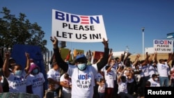 FILE - Migrants from Central America and other nationalities, hoping to cross and request asylum in the U.S., hold banners and shout slogans to U.S. President Joe Biden at their campsite, in Tijuana, Mexico, Feb. 27, 2021.